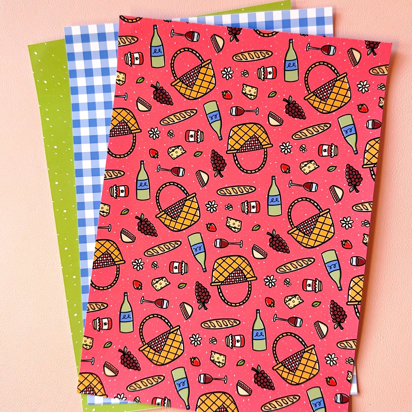 Three sheets of paper with picnic-themed patterns on a pink background