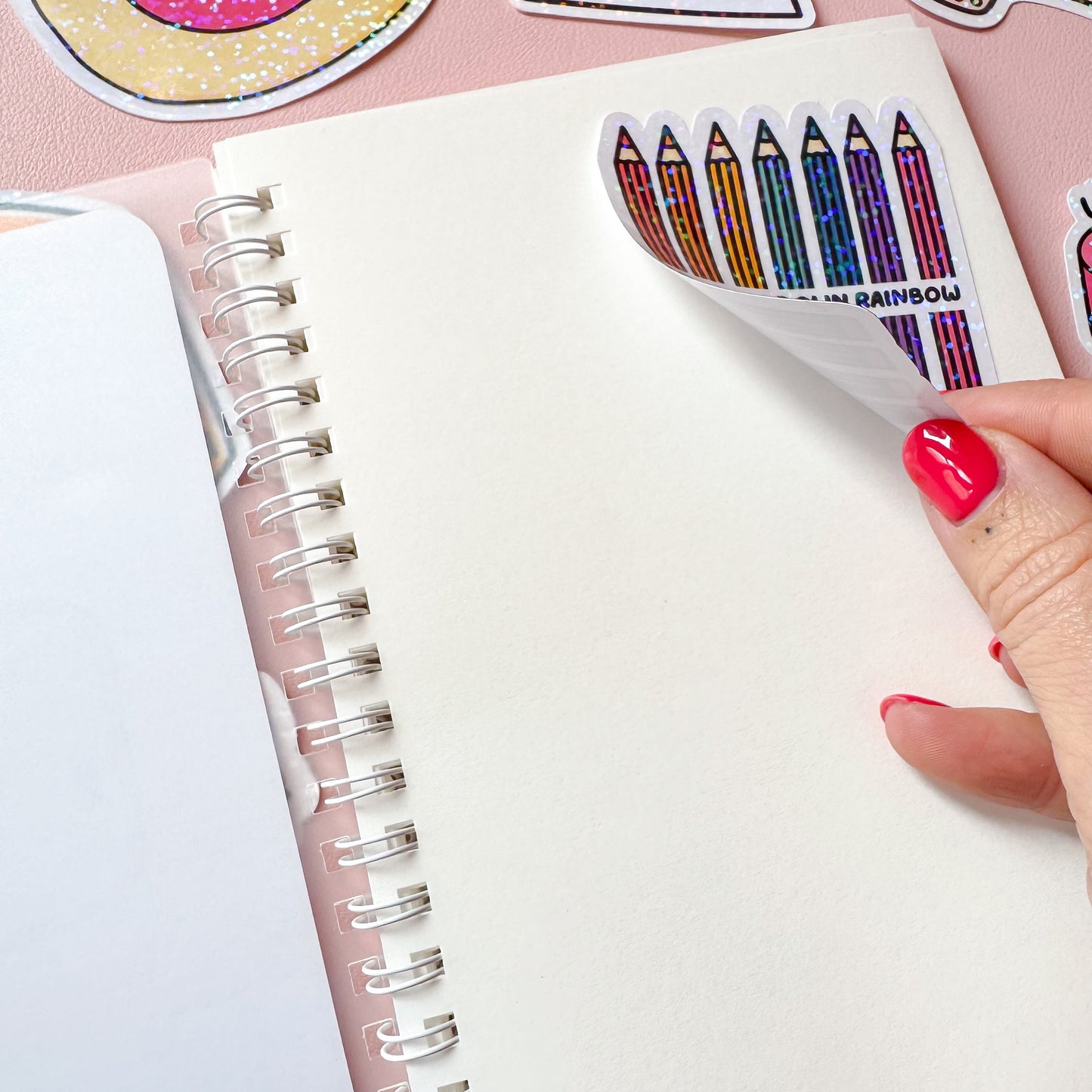 Hand holding a notebook with colorful pencil stickers on a pink background