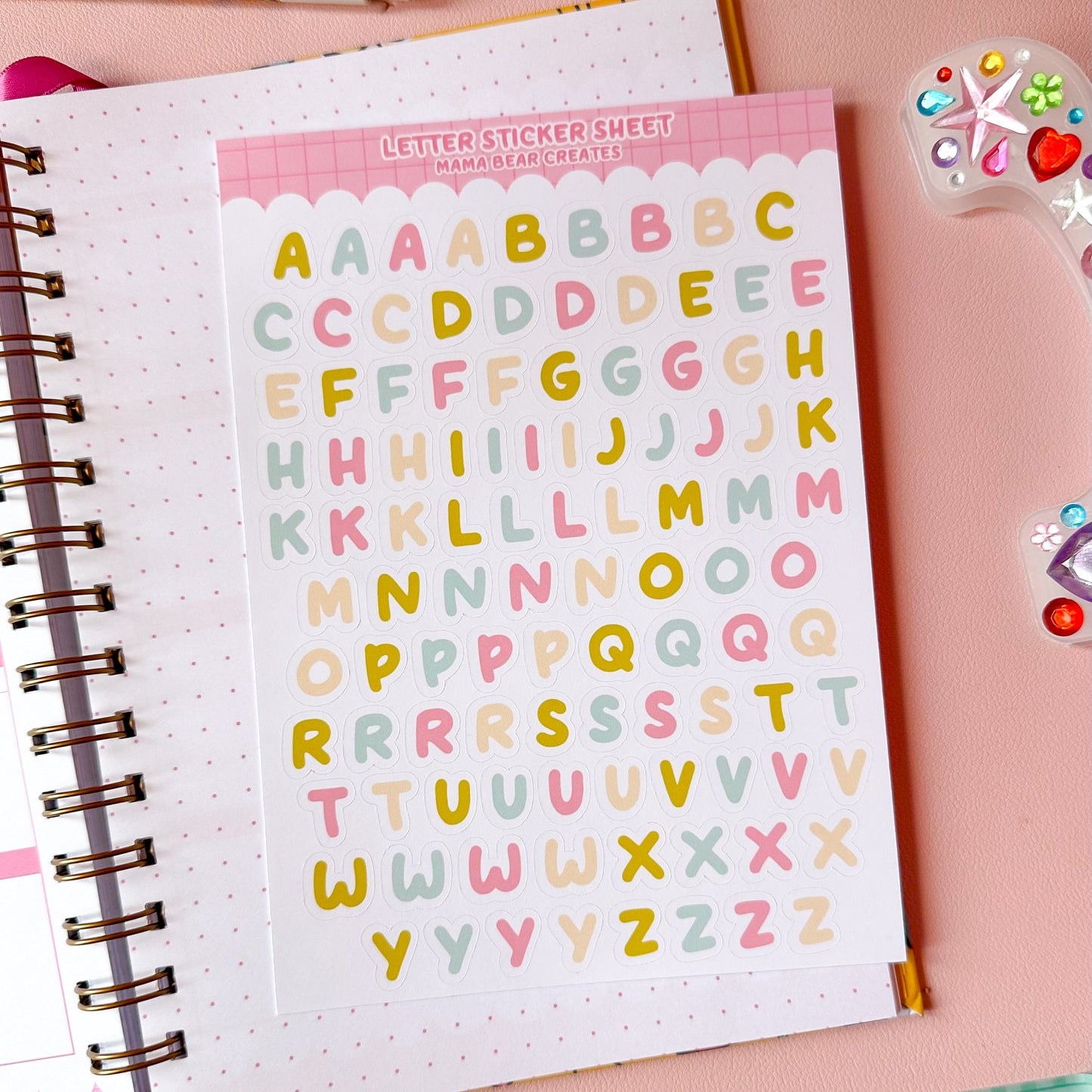 Sheet of colorful alphabet stickers on a notebook with stationery items.