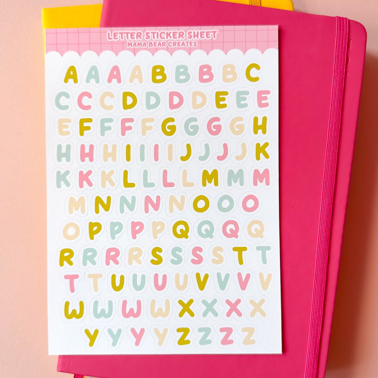 Sheet of colorful letter stickers on a pink notebook with a pink background