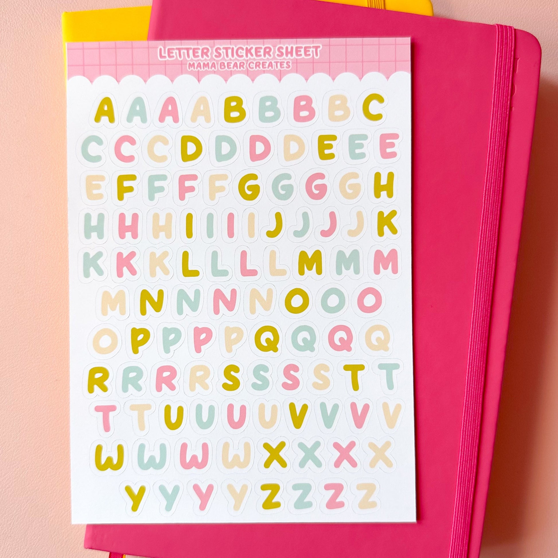 Sheet of colorful letter stickers on a pink notebook with a pink background