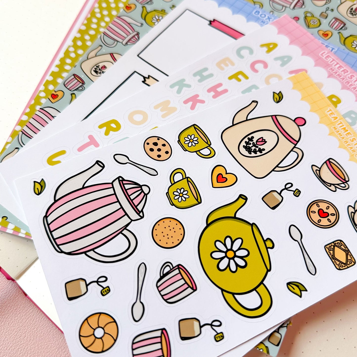 Sheet of colorful tea-themed stickers on a pink surface with other stationery items.