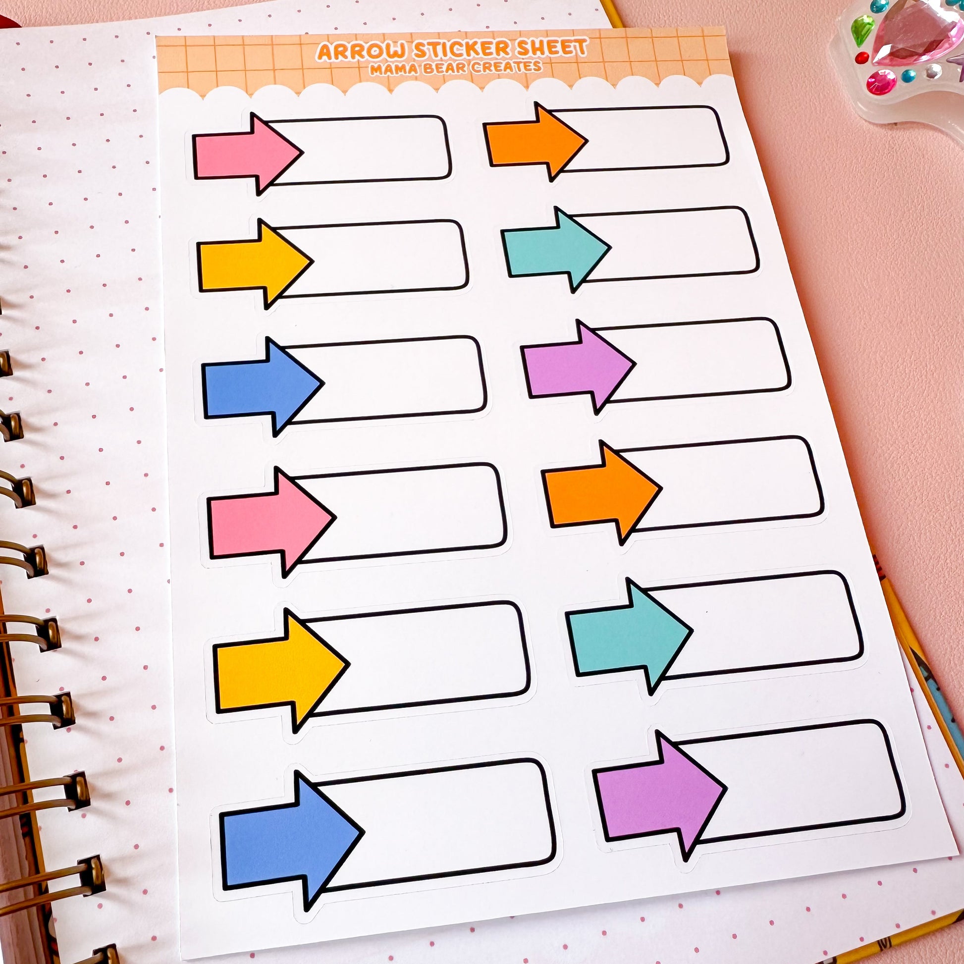 Sheet of colorful arrow stickers on a notebook page with stationery items around.