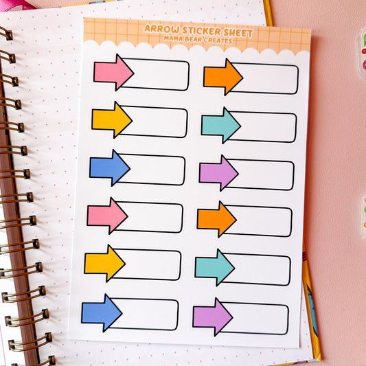Sheet of colorful arrow stickers on a notebook with stationery items around.