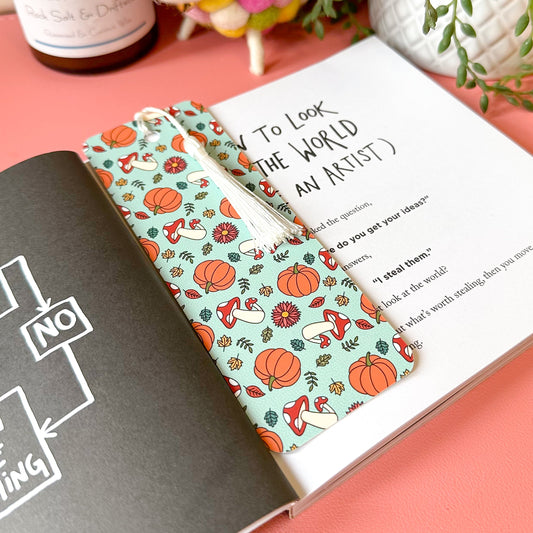 Two colorful bookmarks with autumn designs on a book against a pink background.