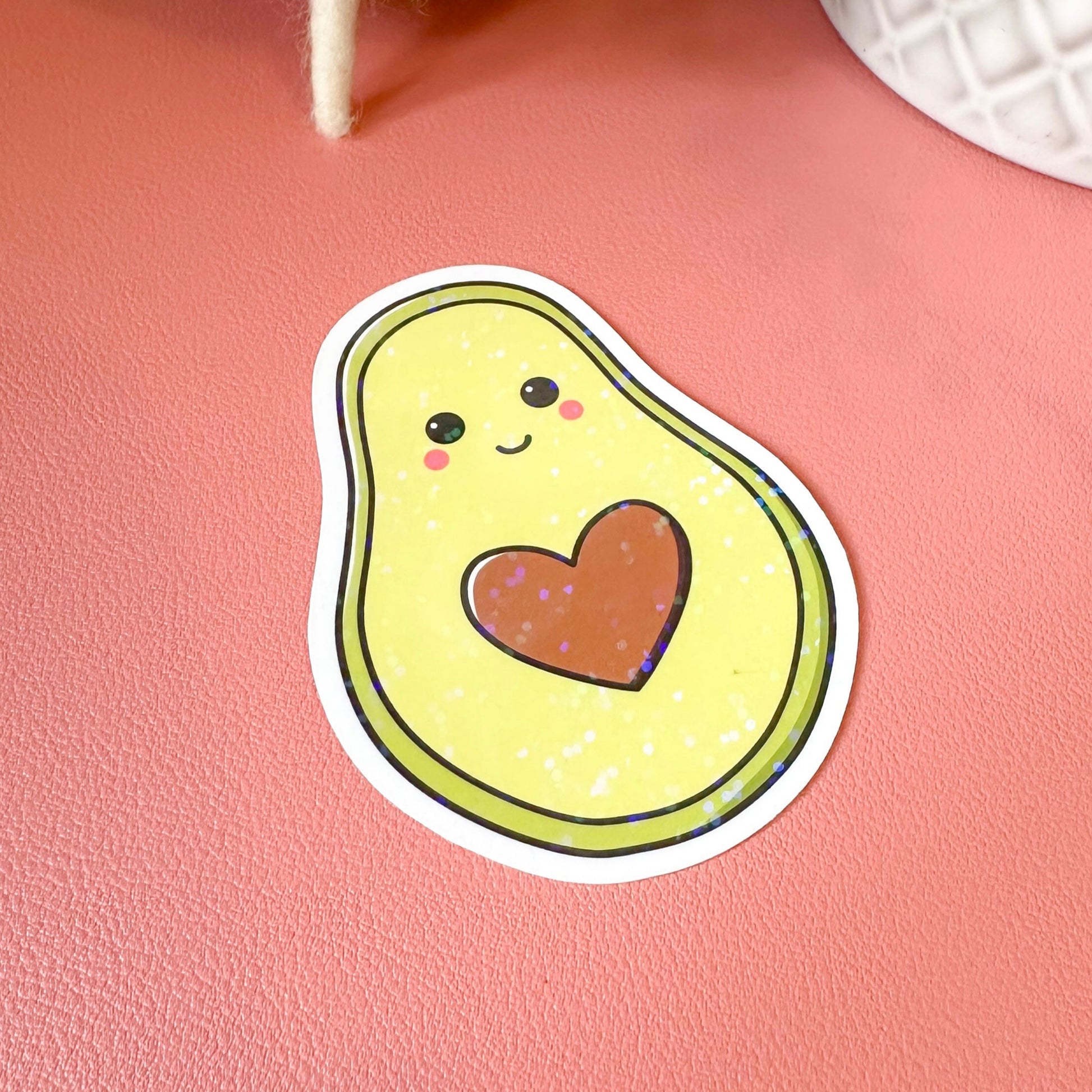 Sticker of a cartoon avocado with a heart on a pink surface