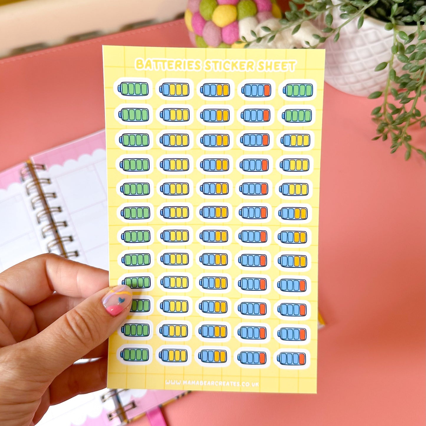 Sheet of colorful stickers held by a hand with a pink background