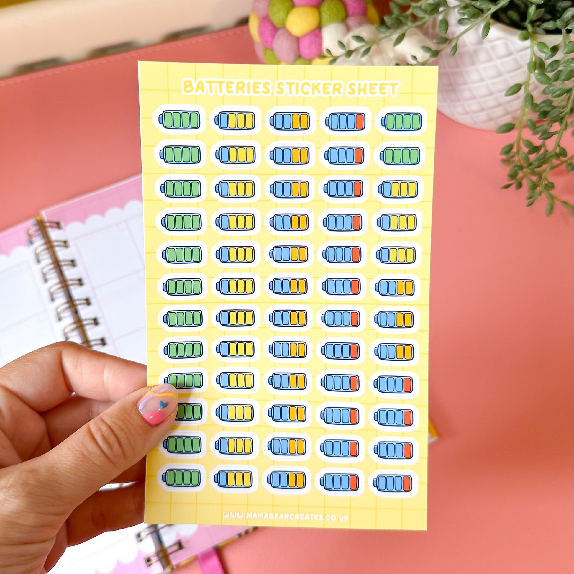 Sheet of colorful stickers held by a hand with a pink background
