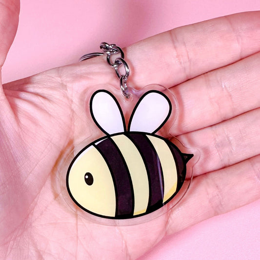 Bee-shaped keychain held in a hand against a pink background