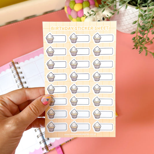 Sheet of birthday-themed stickers with a cupcake design held by a hand on a pink surface.