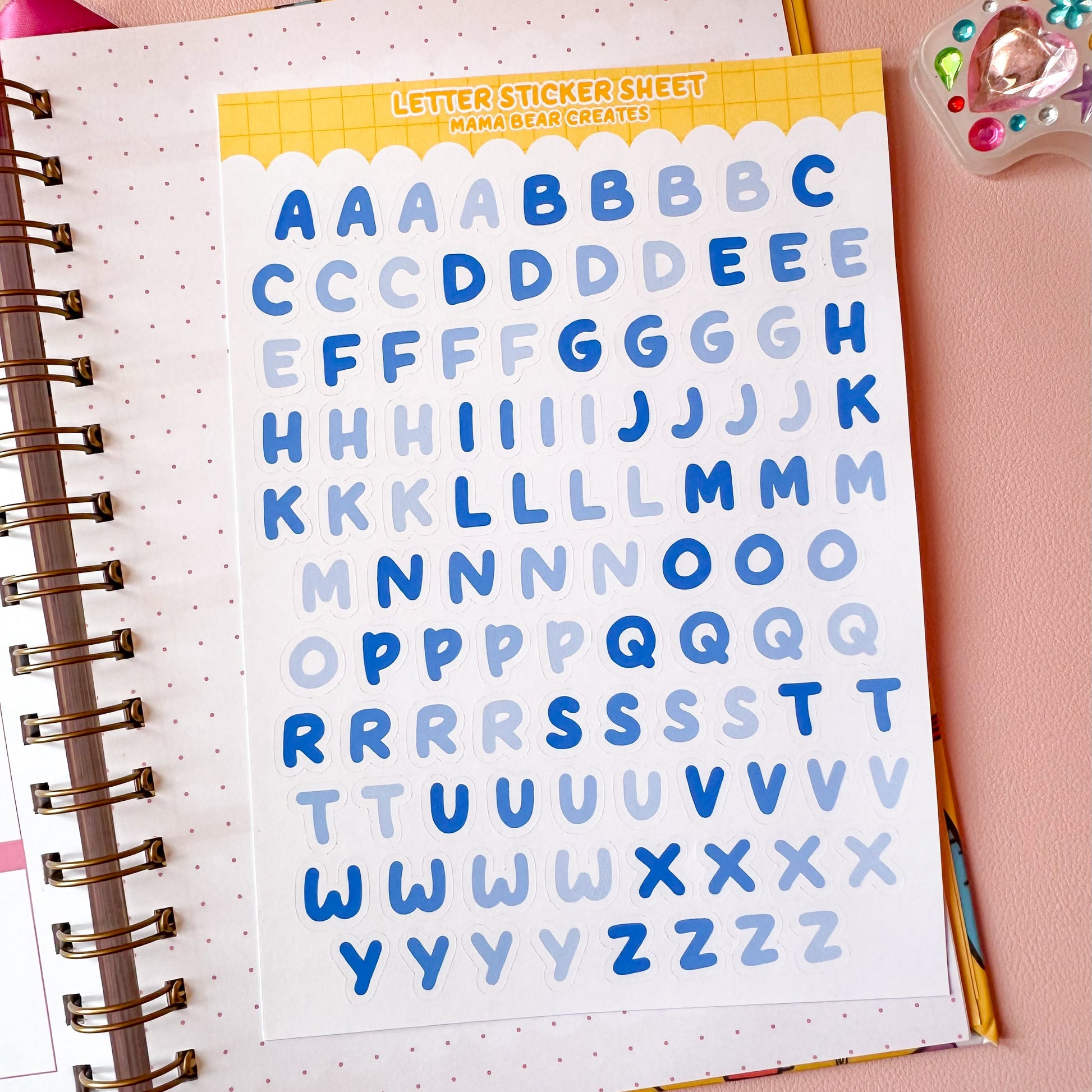 Letter sticker sheet with blue and white letter designs on a pink surface with stationery items.