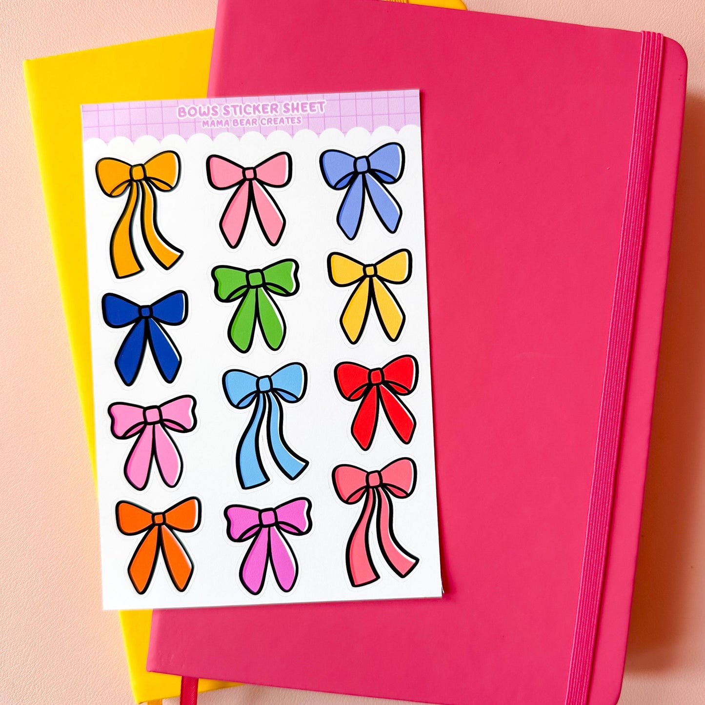Sheet of colorful bow stickers on a pink notebook with a yellow book in the background.