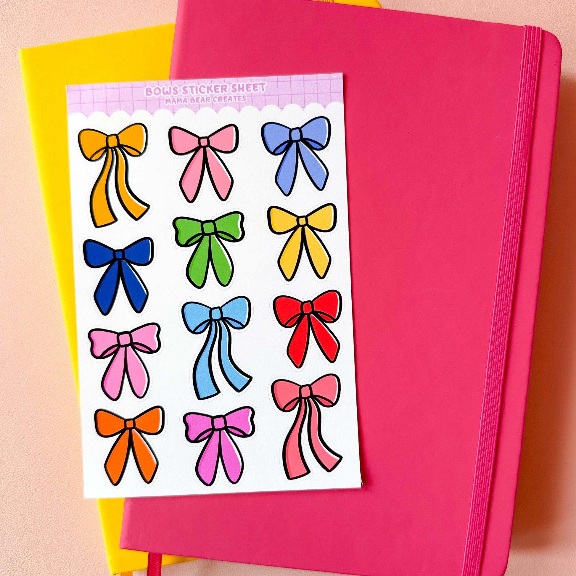 Sheet of colorful bow stickers on a pink notebook with a yellow book in the background.