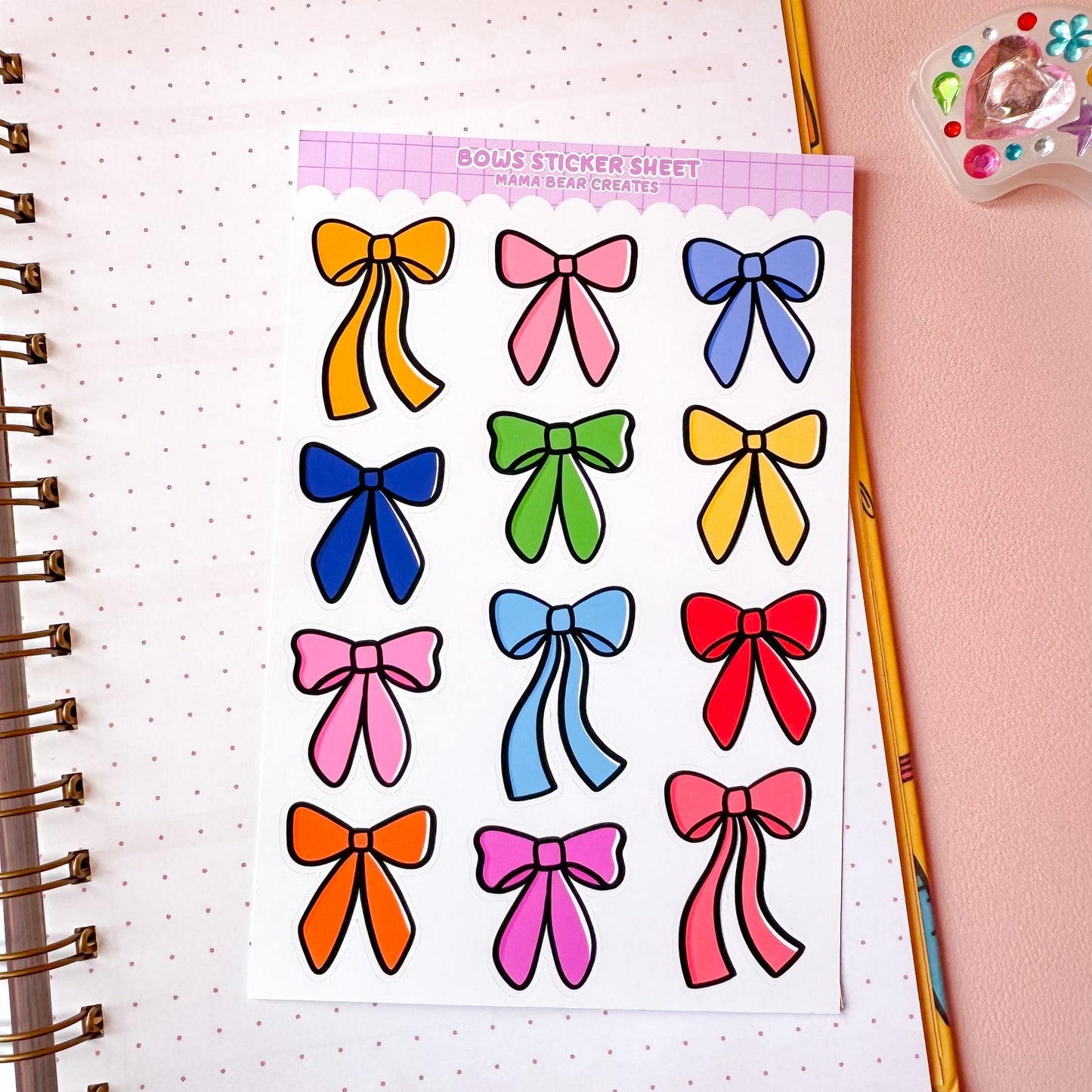 Sheet of colorful bow stickers on a notebook with stationery items.