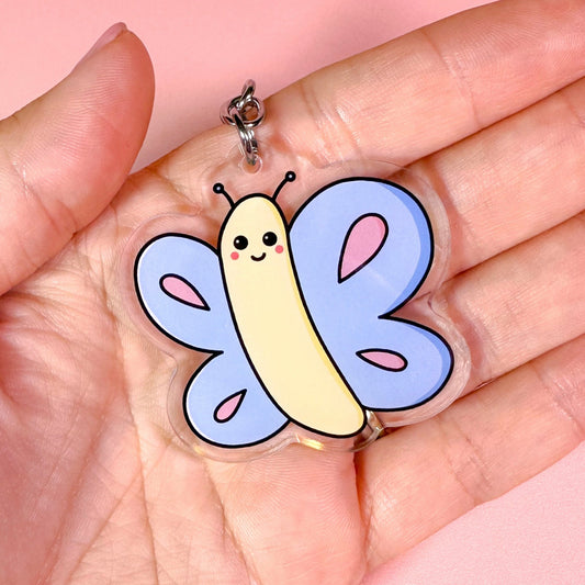 Cartoonish butterfly charm held in a hand against a pink background