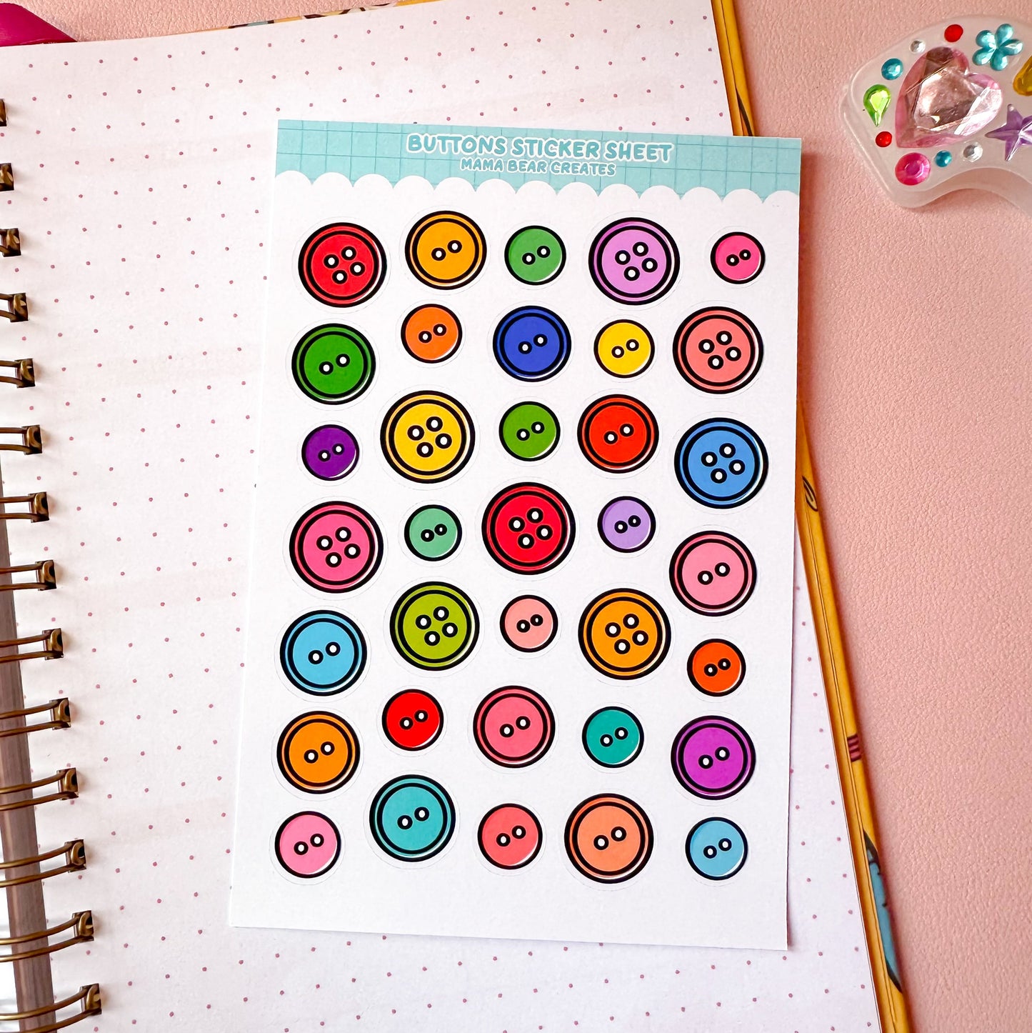 Sheet of colorful button stickers on a notebook with stationery items.