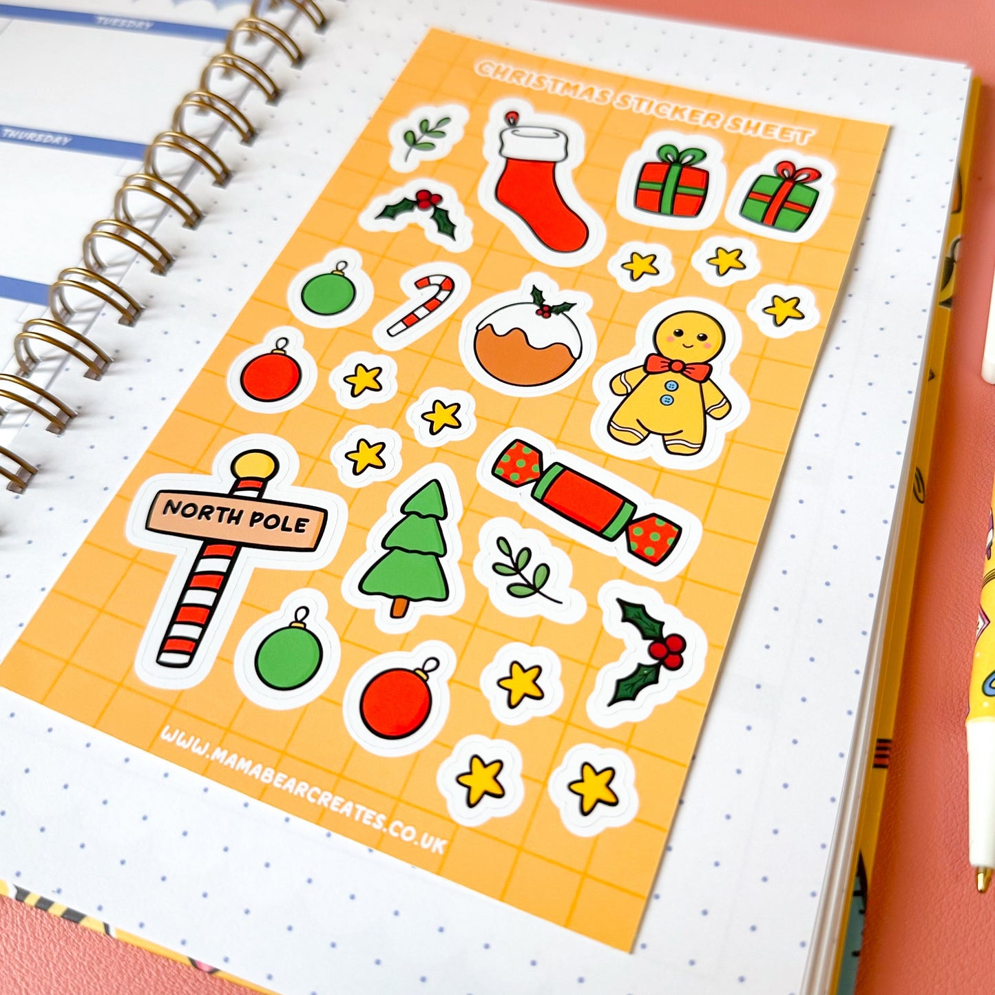 Sheet of Christmas-themed stickers on a notebook with a pen and decorative items.