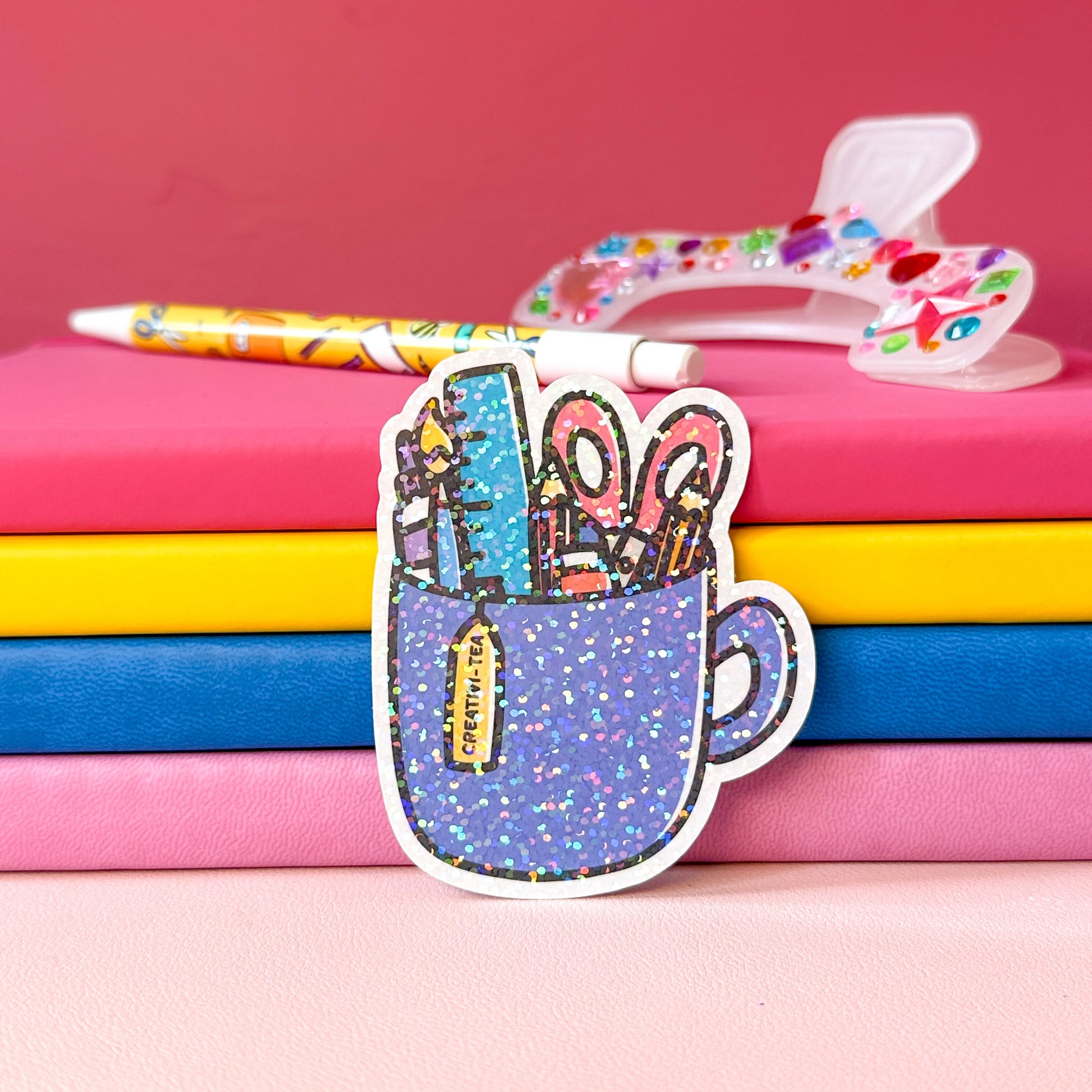 Sticker of a cup with stationery items on colorful books with a pink background