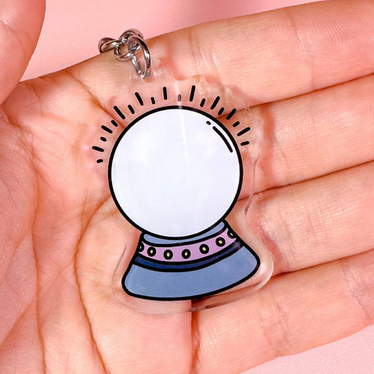 Keychain with a crystal ball design held in a hand against a pink background