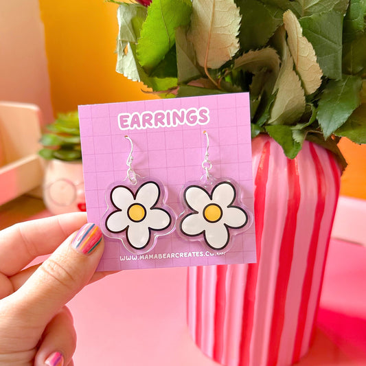 A pair of daisy-shaped earrings in white and yellow, attached to a pink earring card with the text 'EARRINGS' at the top.