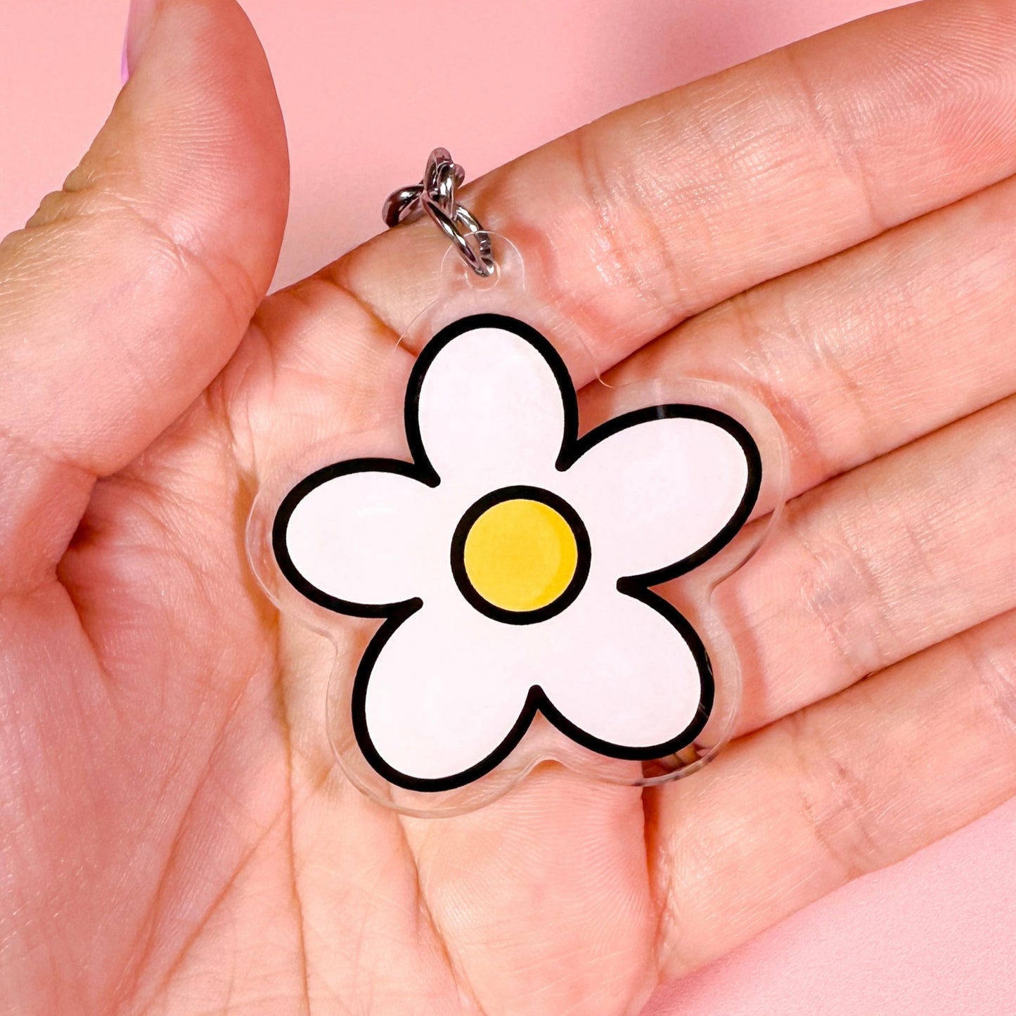 Hand holding a clear charm with a white flower design on a pink background