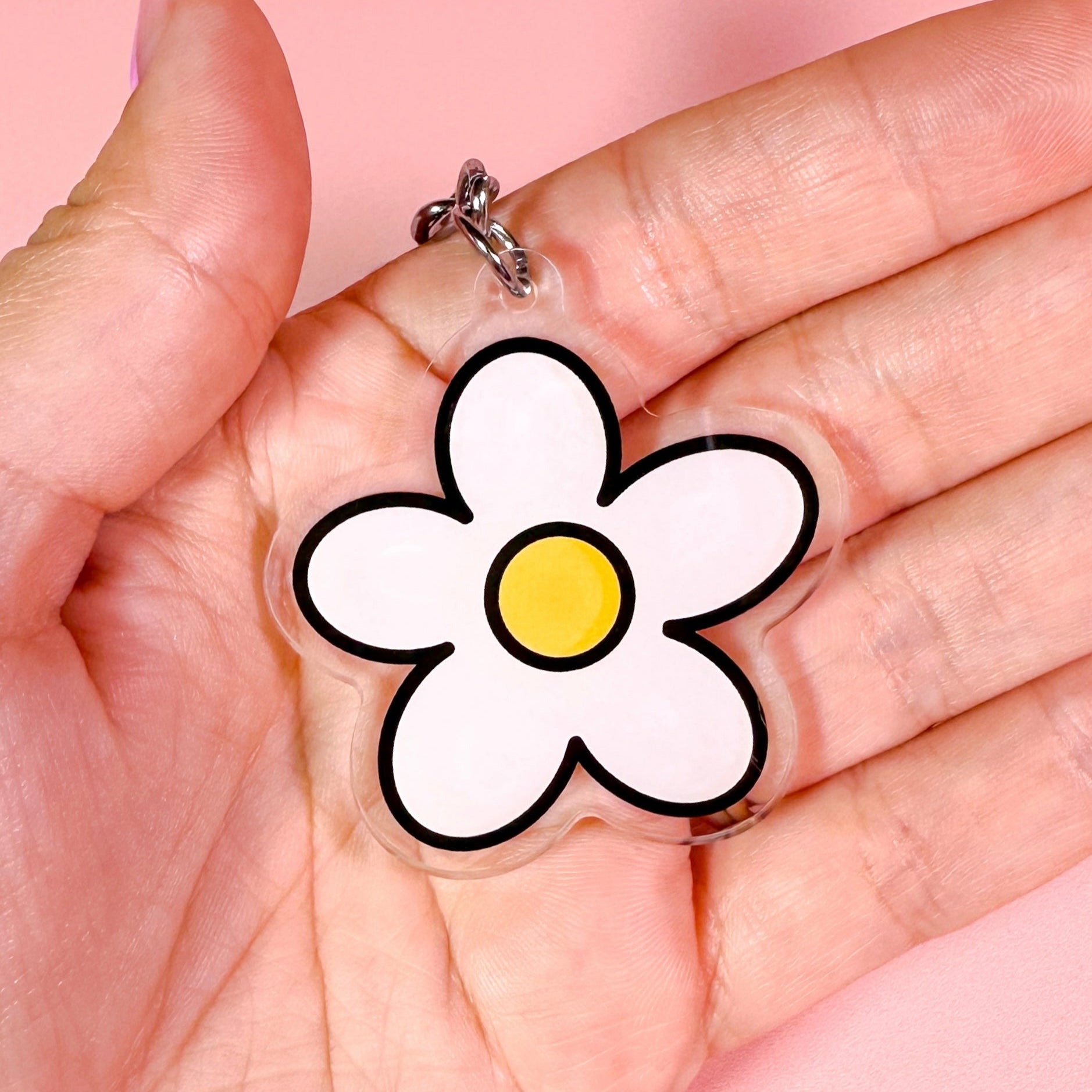 Hand holding a clear charm with a white flower design on a pink background