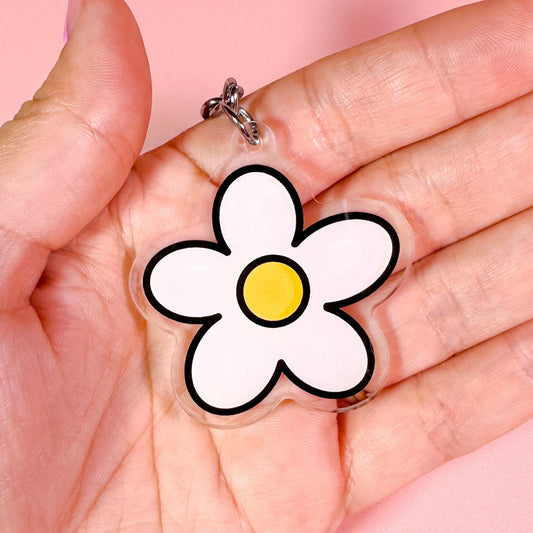 Hand holding a clear charm with a white flower design on a pink background
