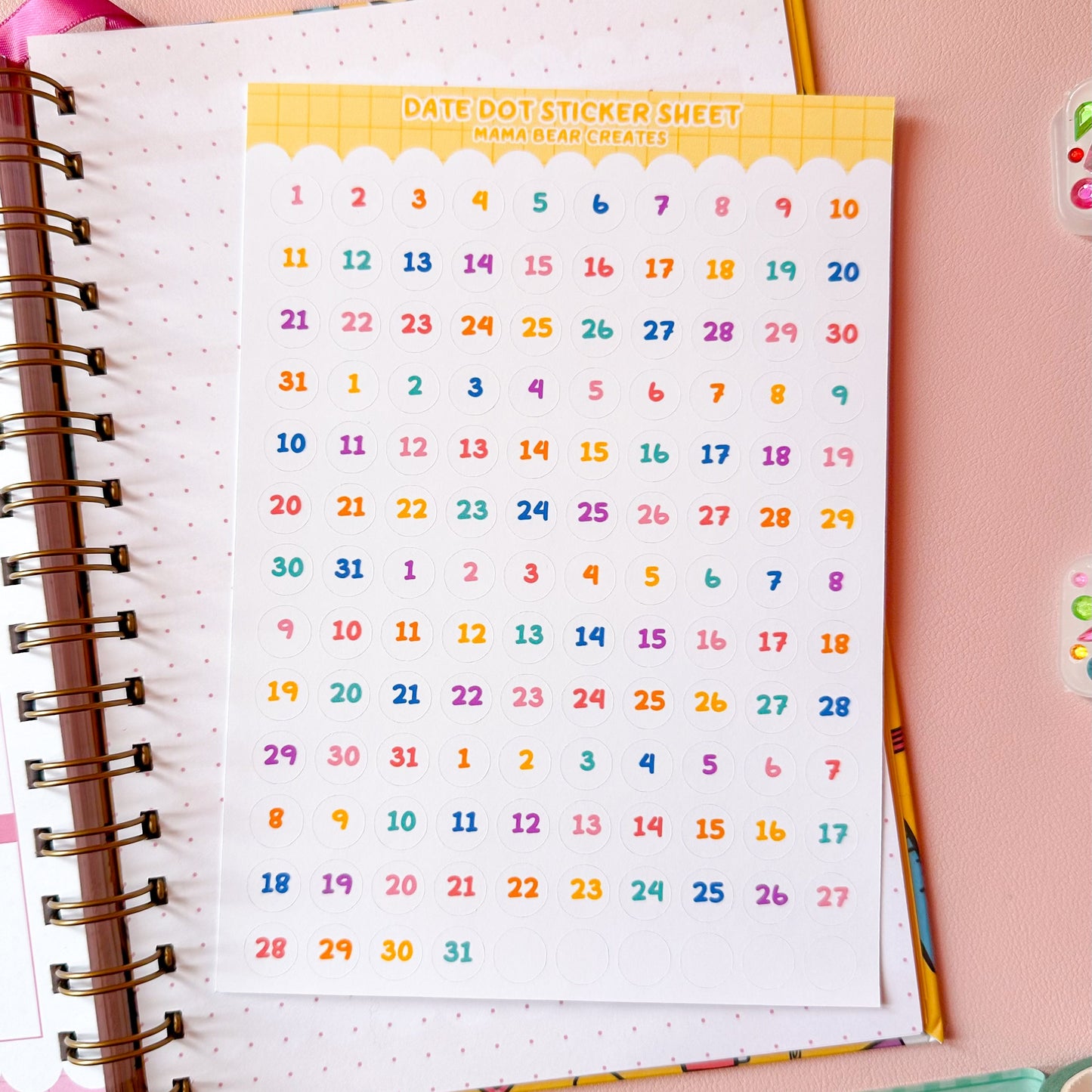 Colorful date dot sticker sheet on a notebook with stationery items on a pink background