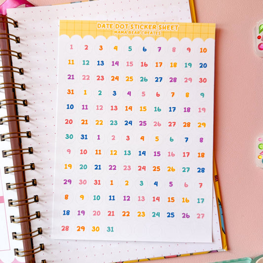 Colorful date dot sticker sheet on a notebook with stationery items on a pink background
