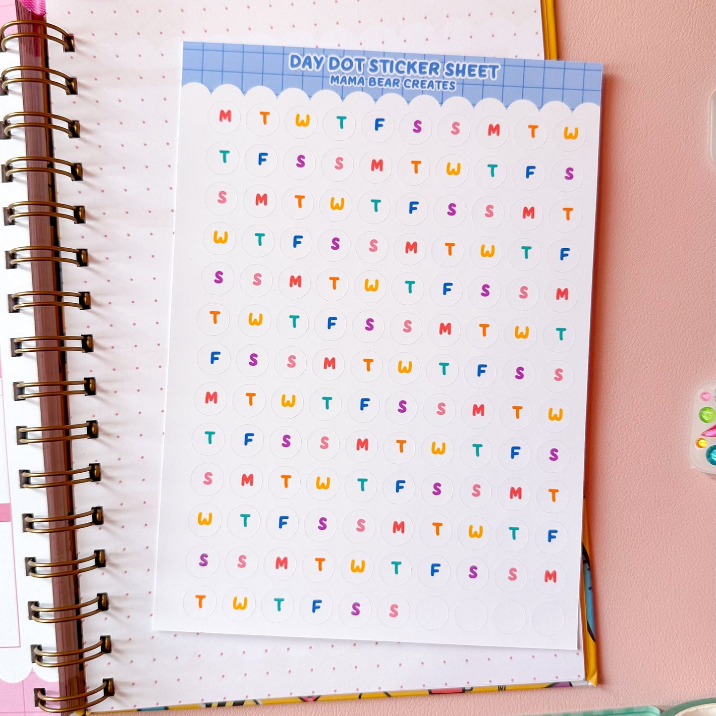 Sheet of colorful letters on a spiral-bound notebook with stationery items on a pink background