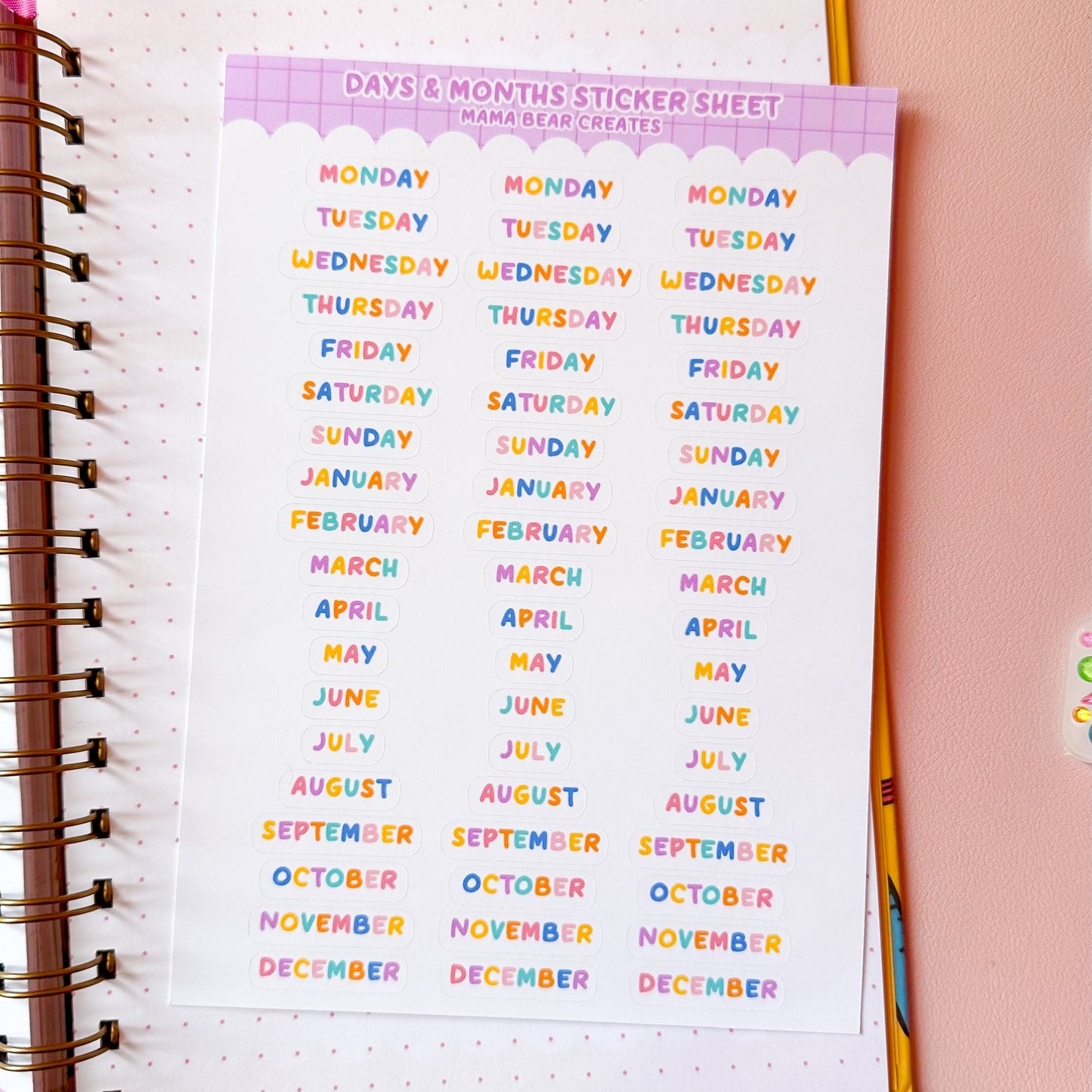 Colorful calendar sticker sheet on a planner with stationery items on a pink background