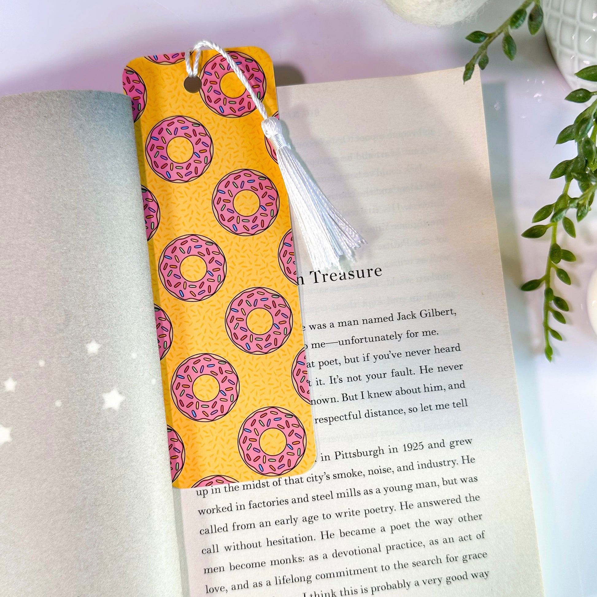A yellow bookmark with pink donut patterns is inserted in an open book. It features rounded corners, a white tassel, and is double-sided.