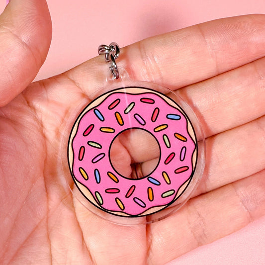 Pink donut charm held in a hand against a pink background