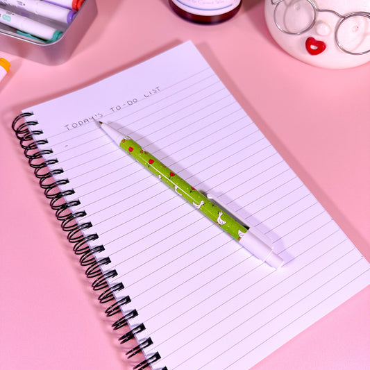 Notebook with a pen on a pink surface with stationery items around