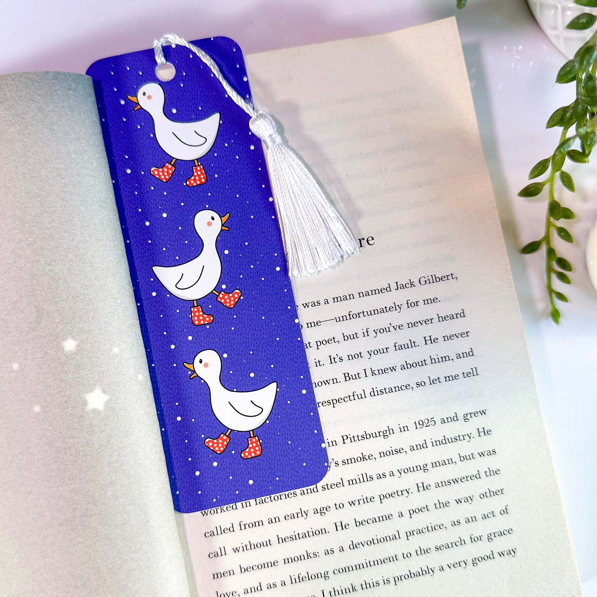 A blue bookmark with illustrations of ducks and a white tassel, placed in an open book.