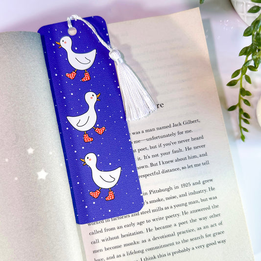 A blue bookmark with illustrations of ducks and a white tassel, placed in an open book.