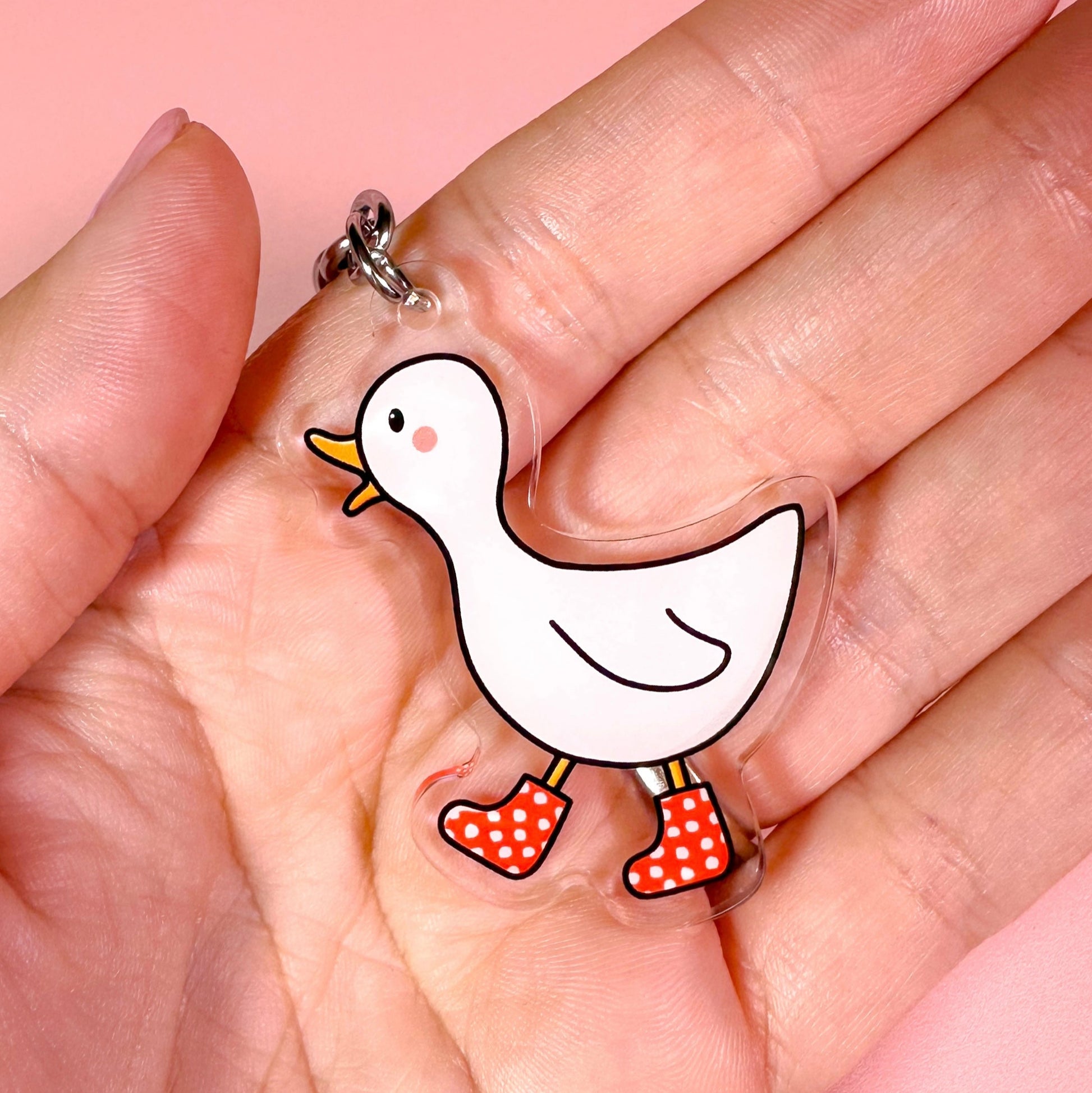 Cartoon duck keychain held in a hand against a pink background