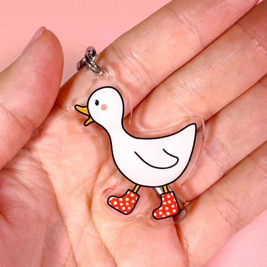Cartoon duck keychain held in a hand against a pink background