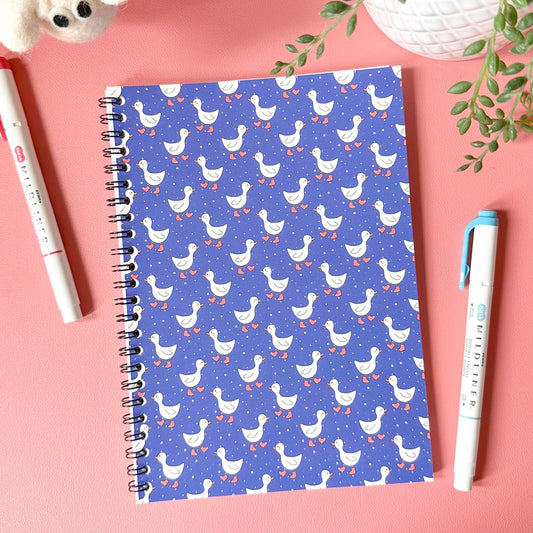 Notebook with duck pattern on a pink surface with pens and plants