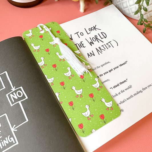 Book with a green bookmark featuring duck and tulip pattern on a pink surface.