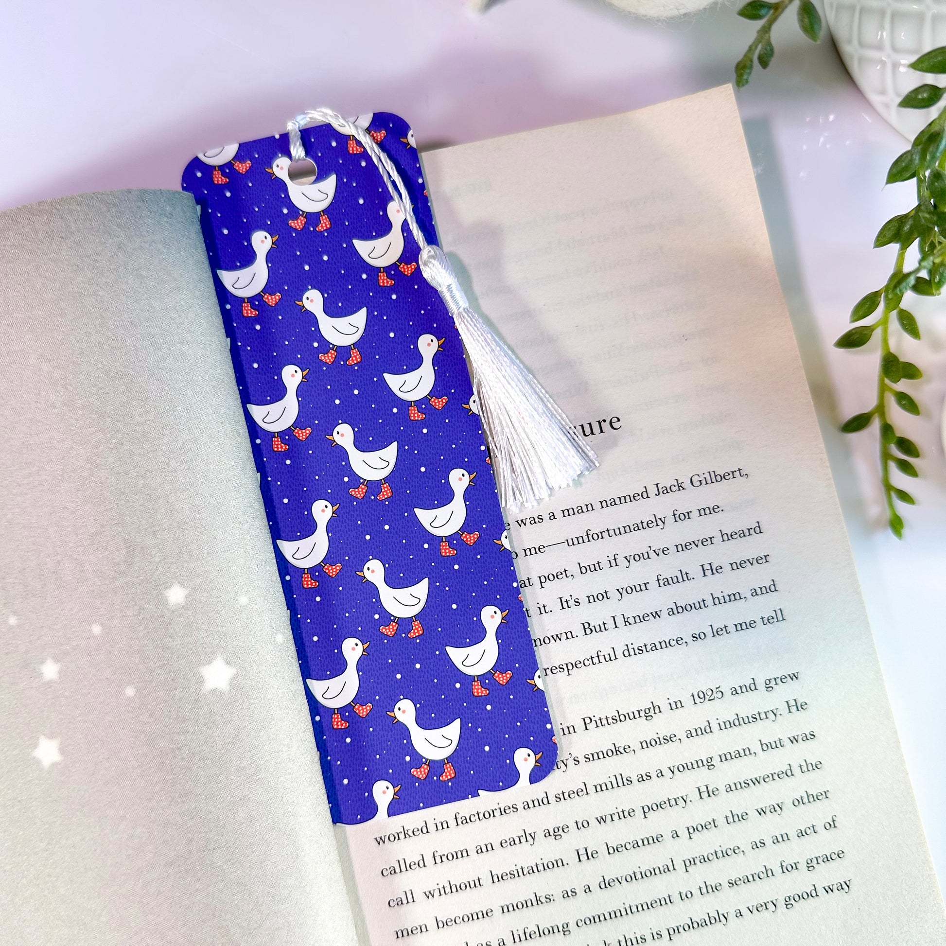 A blue bookmark with a pattern of white ducks, and a white tassel, placed in an open book.