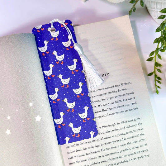 A blue bookmark with a pattern of white ducks, and a white tassel, placed in an open book.