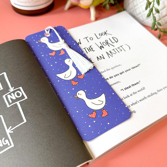 Book with a blue bookmark featuring cartoon ducks on a pink surface
