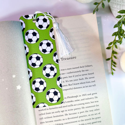 A green bookmark with white football patterns and a white tassel, placed in an open book.