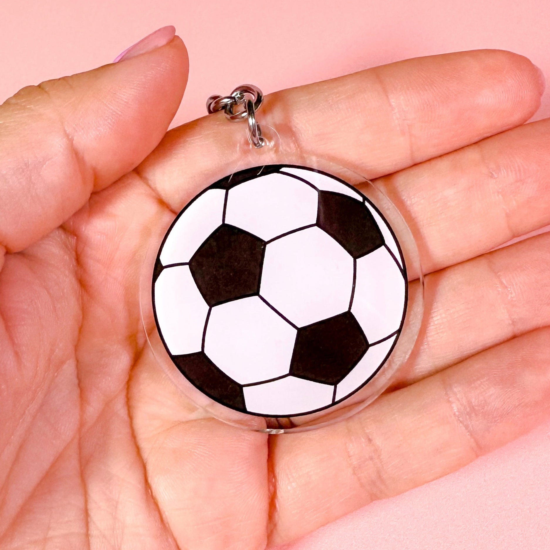 football pendant held in a hand against a pink background