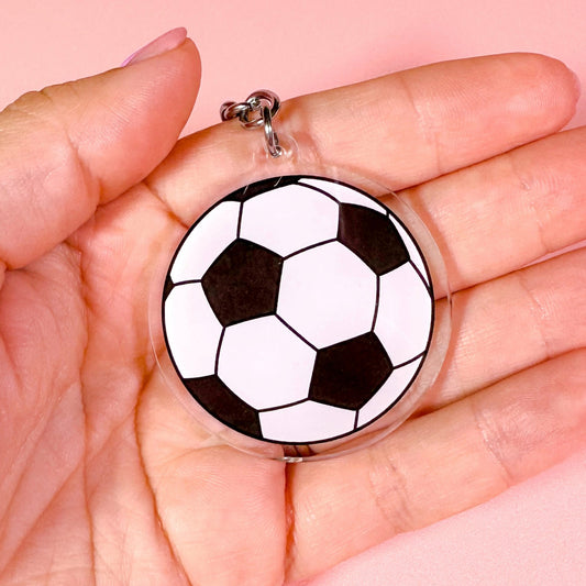 football pendant held in a hand against a pink background
