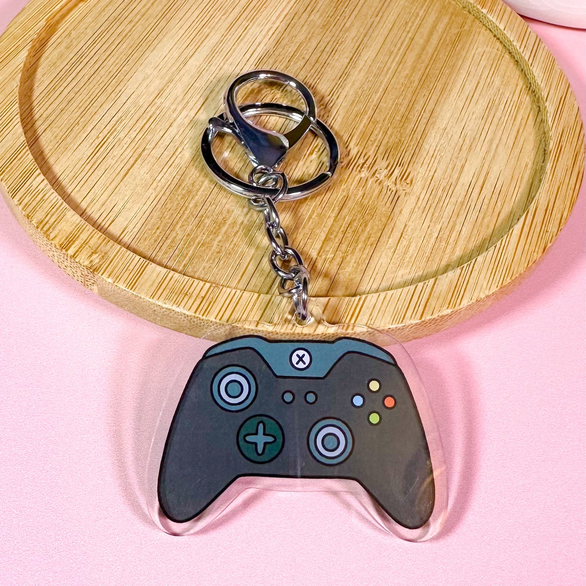 Keychain shaped like a gaming controller on a pink surface with a wooden coaster.