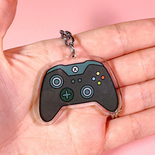 Gaming controller keychain held in a hand against a pink background