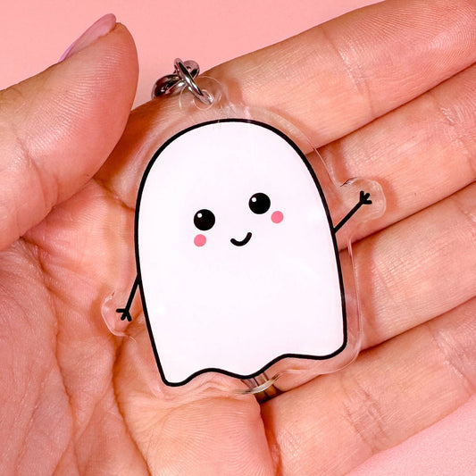 Hand holding a cute ghost-shaped keychain against a pink background
