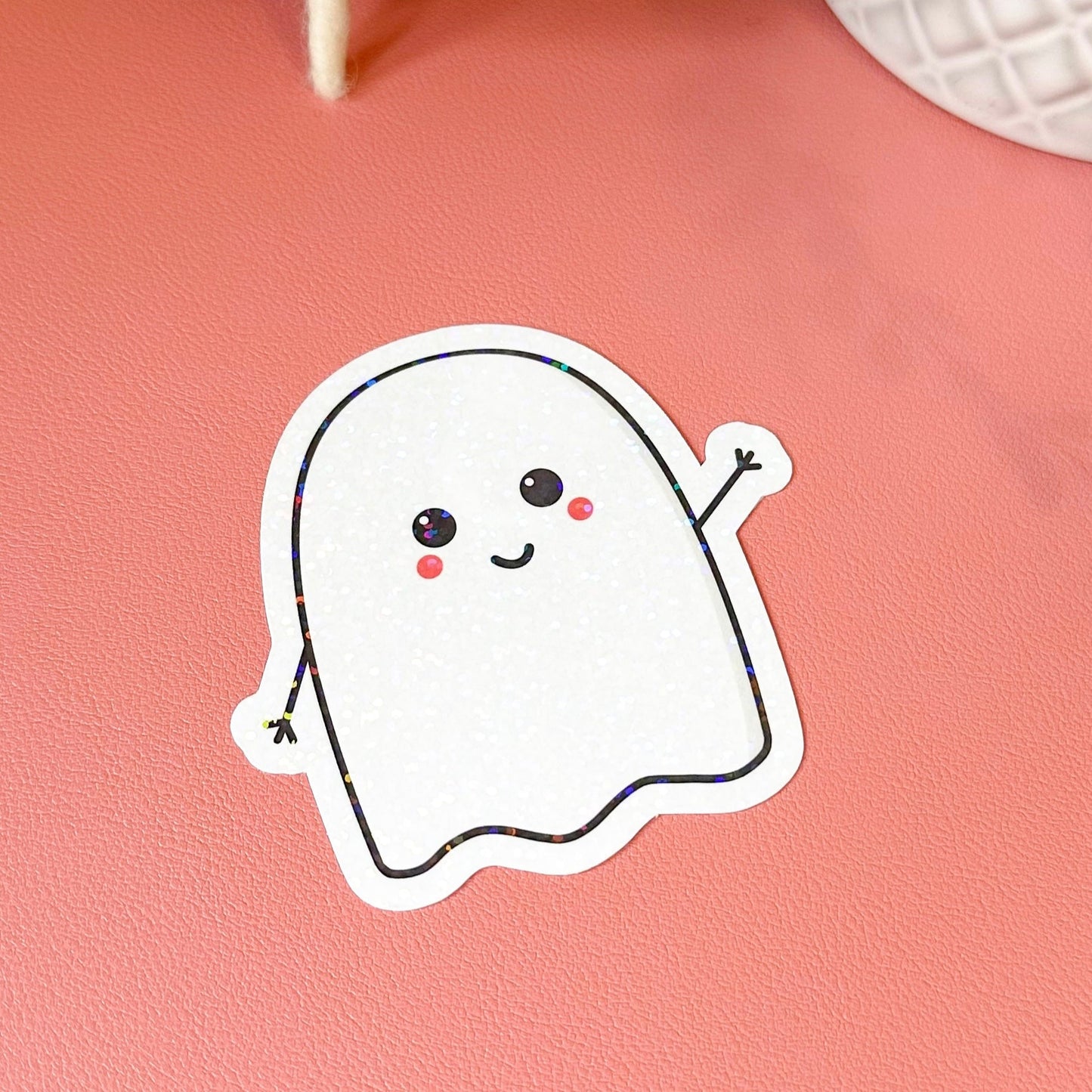 Cartoon ghost sticker on a pink surface with decorative items in the background
